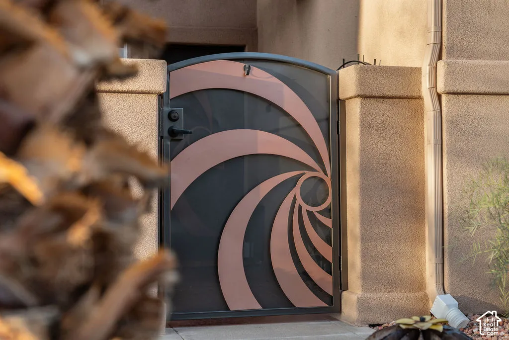 Custom arched security gate featuring geometric metal detailing, a metallic finish, and reinforced hardware set within a textured stucco perimeter wall