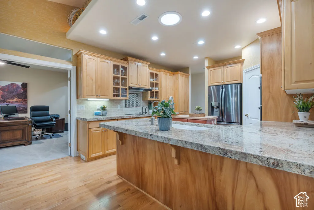 Kitchen featuring light wood cabinetry, stone countertops, an island with an integrated sink, recessed lighting, and wood-finish flooring