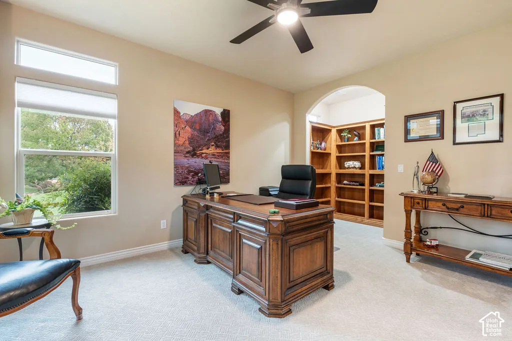 Room featuring natural light, custom built-in wood shelving, an arched entryway, and a ceiling fan