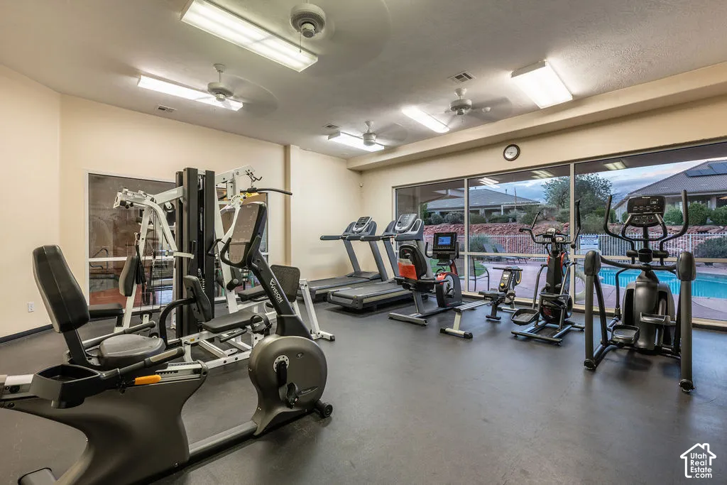 Fitness center featuring rubber flooring, ceiling-mounted fluorescent lighting, dual ceiling fans, and expansive floor-to-ceiling windows