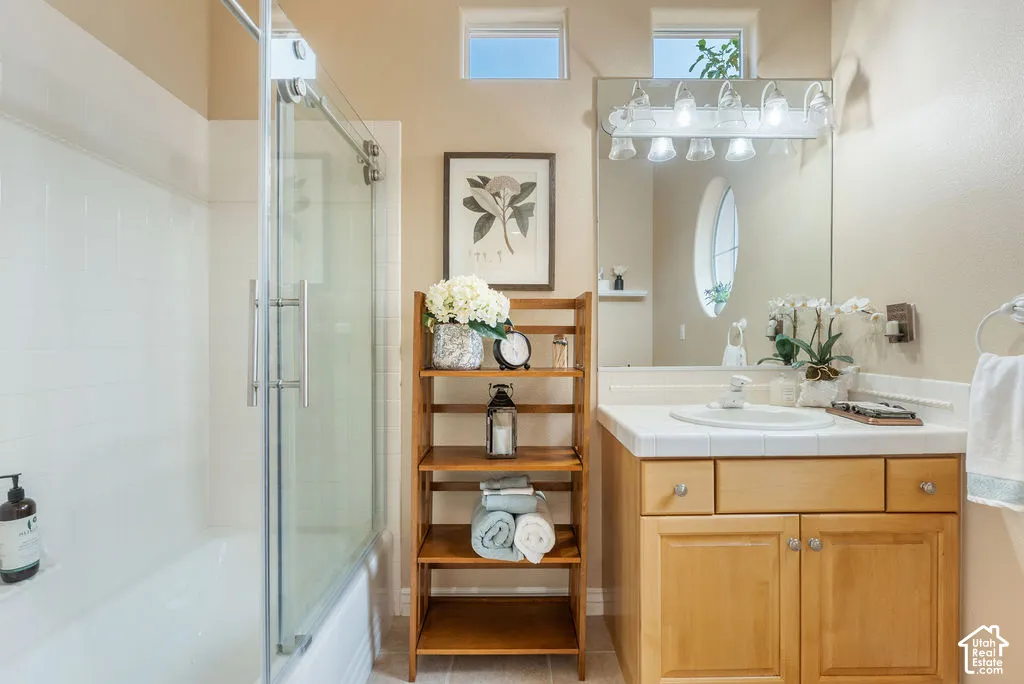 Bathroom featuring a vanity with wood cabinetry, a tiled countertop, and a glass-enclosed shower