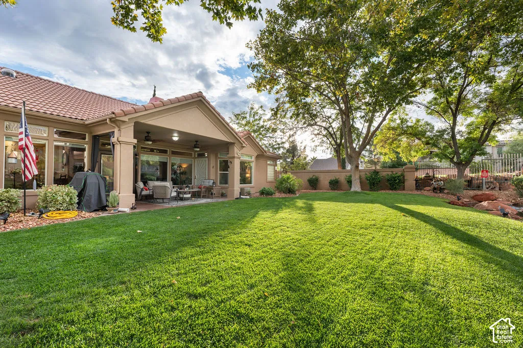 Backyard featuring a covered patio, extensive grass lawn, mature trees, and a masonry perimeter wall
