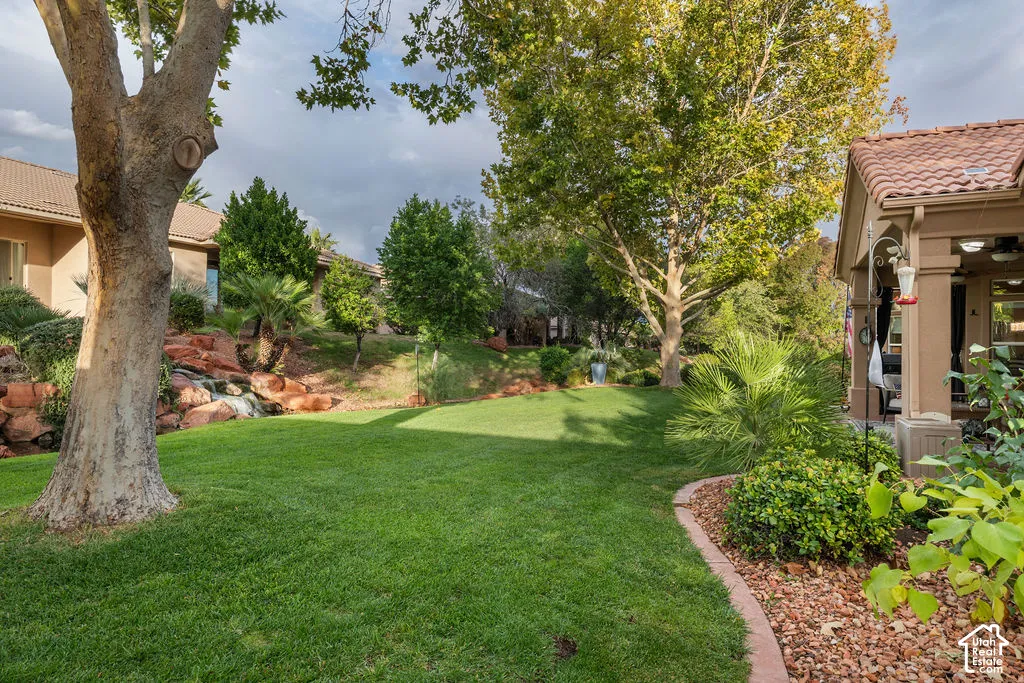 Landscaped backyard featuring a manicured lawn, tiered natural rock accents, mature trees, and a covered patio with a tile roof