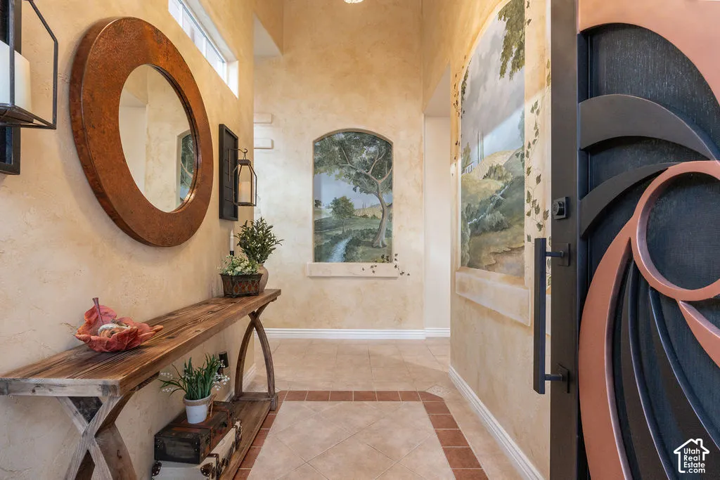 Custom entry door featuring geometric metal detailing, textured wall finishes, tile flooring with decorative borders, and an inset wall mural