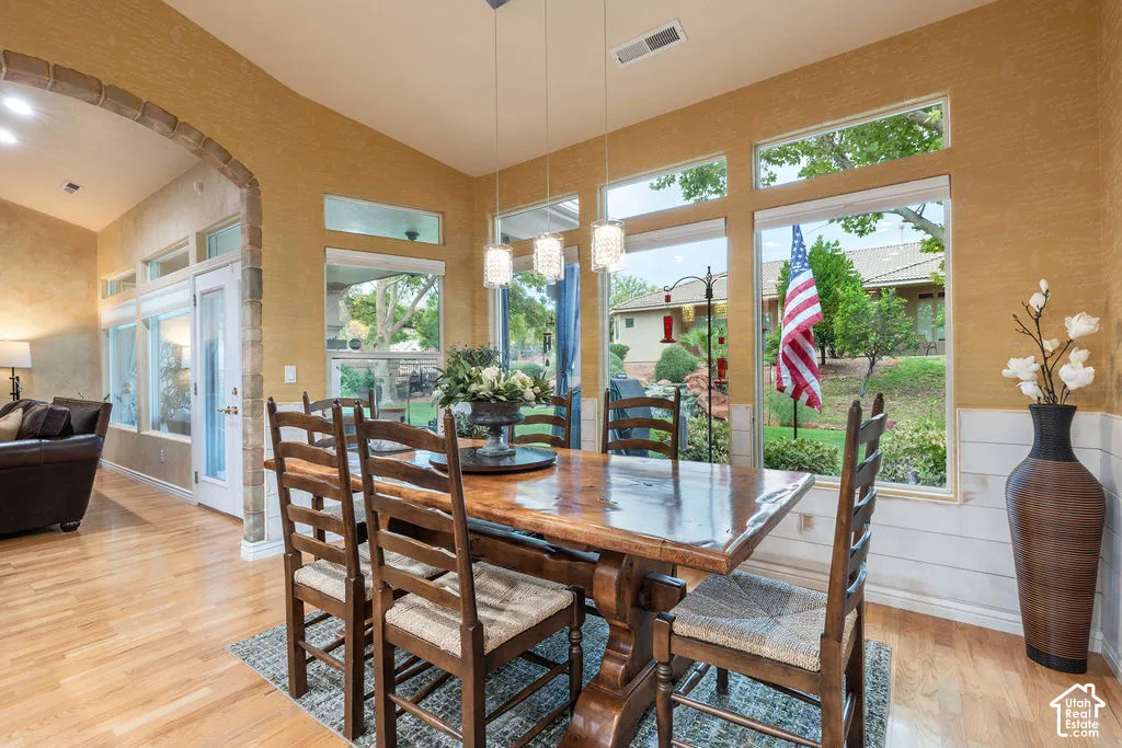 Dining area featuring wood-finish flooring, a stone-accented arched entryway, white horizontal wainscoting, triple pendant lighting, and oversized windows