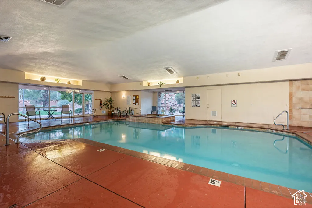 Indoor swimming pool area featuring a recessed hot tub, floor-to-ceiling glass windows, and metal handrails