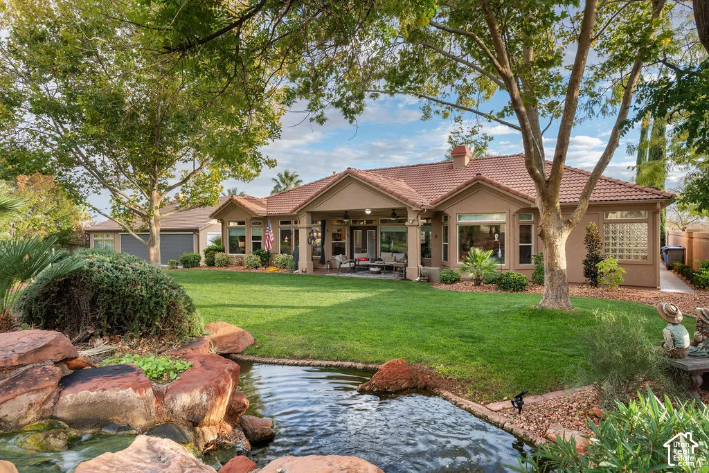 Rear exterior featuring a tile roof, covered patio, integrated rock-feature pond, mature trees, and manicured lawn