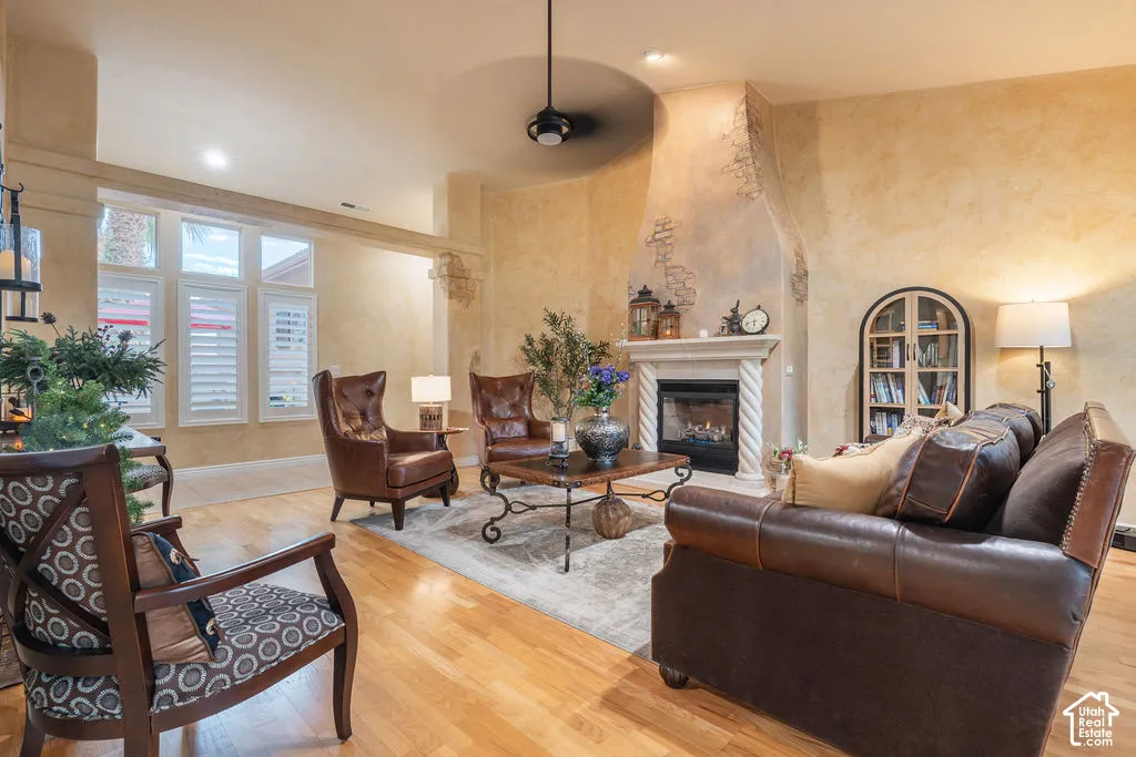 Living area featuring vaulted ceilings, wood-finish flooring, a fireplace with a decorative mantel and stone-textured surround, plantation shutters, and a built-in arched display cabinet
