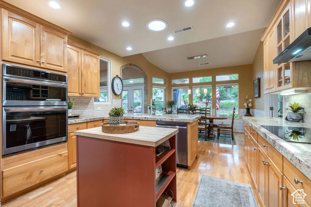 Kitchen featuring light wood cabinetry, stone countertops, stainless steel double wall ovens, wood-finish flooring, and a central island with a wood countertop