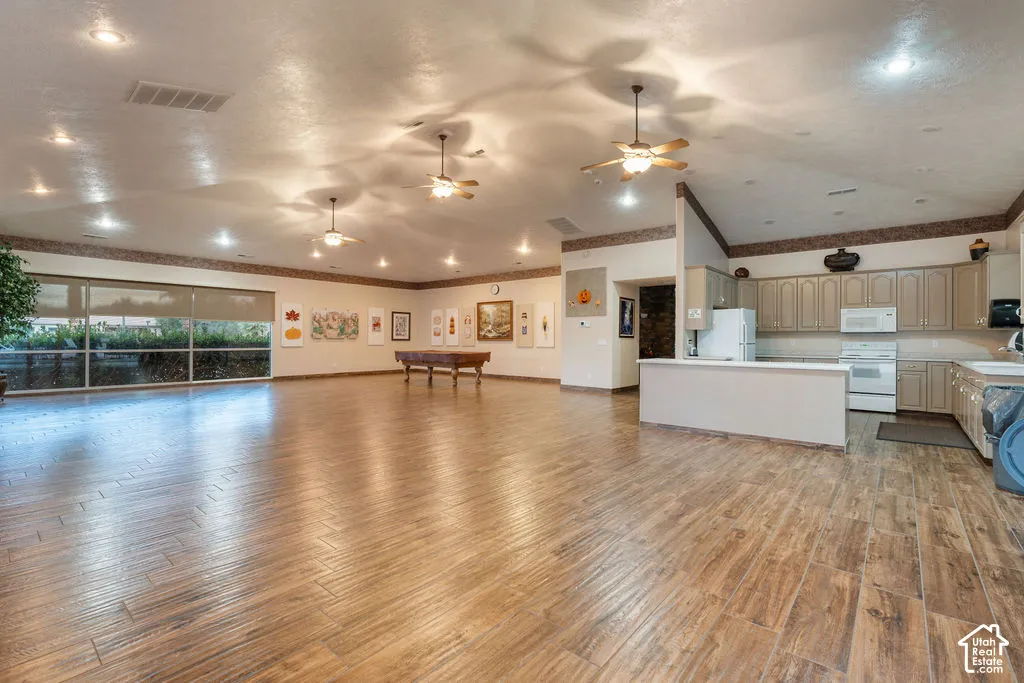Expansive open-concept space multipurpose room in the clubhouse featuring wood-finish flooring, vaulted ceilings with multiple ceiling fans, recessed lighting, and a kitchen equipped with cabinetry and a peninsula counter