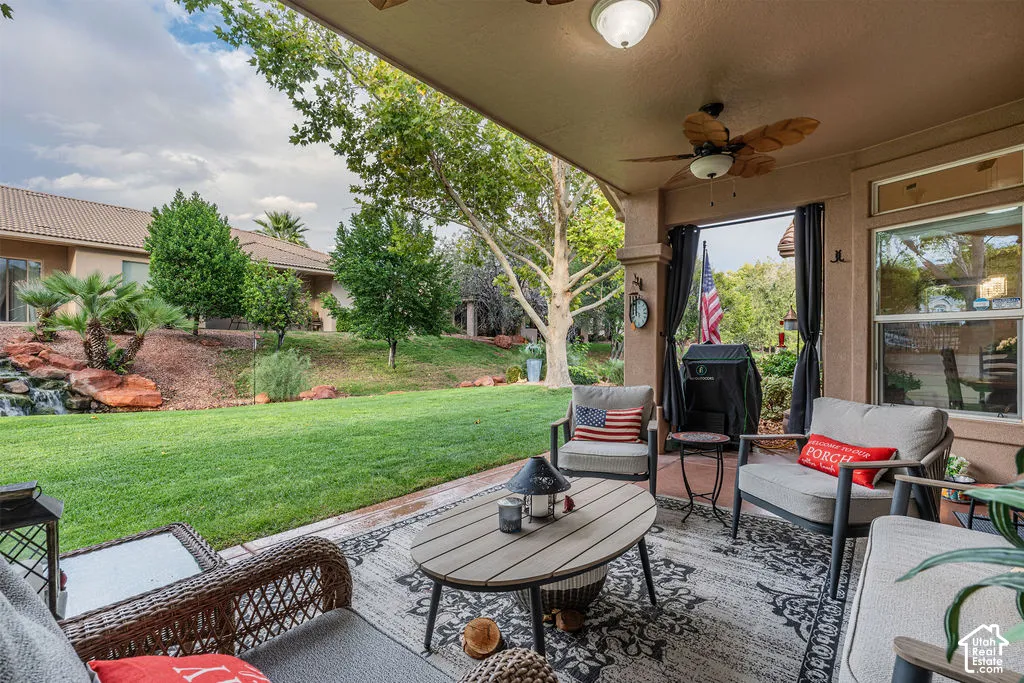 Covered patio featuring a ceiling fan and exterior lighting, overlooking a manicured lawn with mature trees and a stone-accented water feature