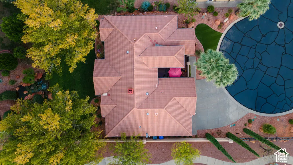 Aerial perspective of a property featuring a tile roof, paved circular driveway, landscaped grounds with mature trees, and synthetic lawn areas