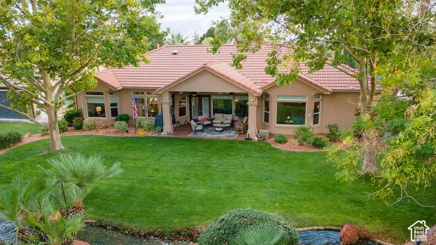 Exterior rear view featuring a tile roof, covered patio, manicured lawn, mature trees, and landscaping with a water feature