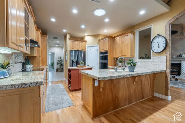 Kitchen featuring light wood cabinetry, stone countertops, stainless steel double wall ovens, a central island with decorative corbels, and recessed lighting