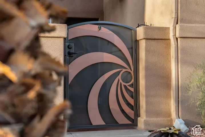 Custom arched security gate featuring geometric metal detailing, a metallic finish, and reinforced hardware set within a textured stucco perimeter wall