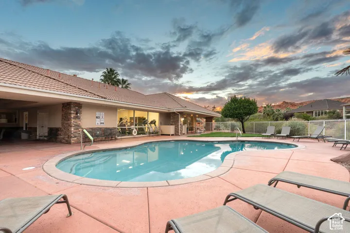 Freeform swimming pool with concrete decking, tile roof, stone masonry accents, and a metal perimeter fence