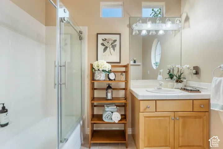 Bathroom featuring a vanity with wood cabinetry, a tiled countertop, and a glass-enclosed shower
