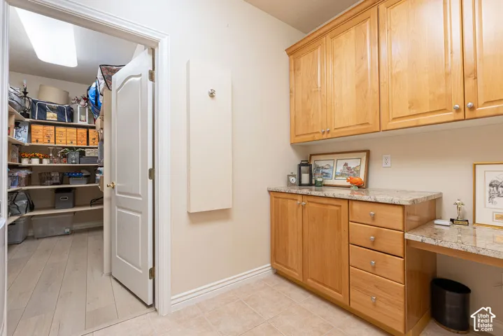Custom cabinetry with stone-finish countertops, tile flooring, and walk-in pantry featuring built-in shelving