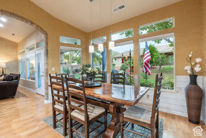 Dining area featuring wood-finish flooring, a stone-accented arched entryway, white horizontal wainscoting, triple pendant lighting, and oversized windows