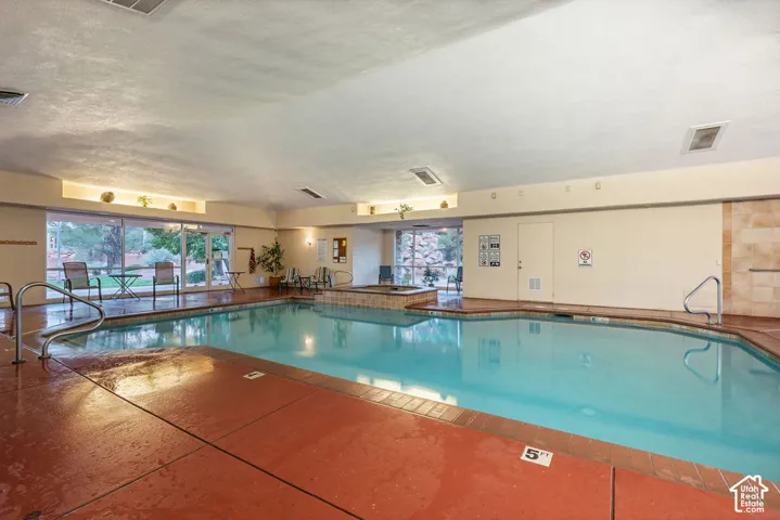 Indoor swimming pool area featuring a recessed hot tub, floor-to-ceiling glass windows, and metal handrails