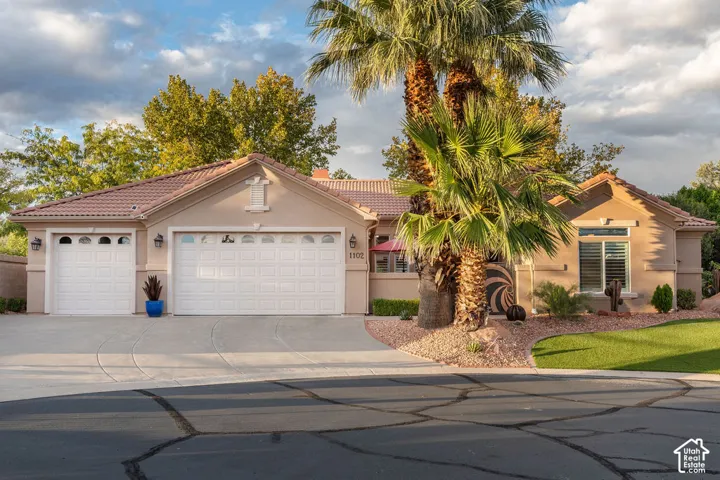 Stucco exterior featuring a multi-car garage, clay tile roof, mature palm landscaping, and stone-accented front grounds