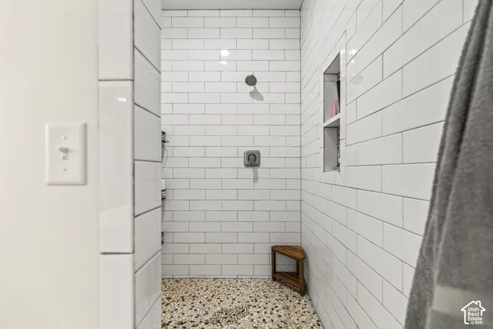 Walk-in shower featuring white subway tile walls, a pebble-finish floor, a recessed wall niche, and a wall-mounted shower fixture