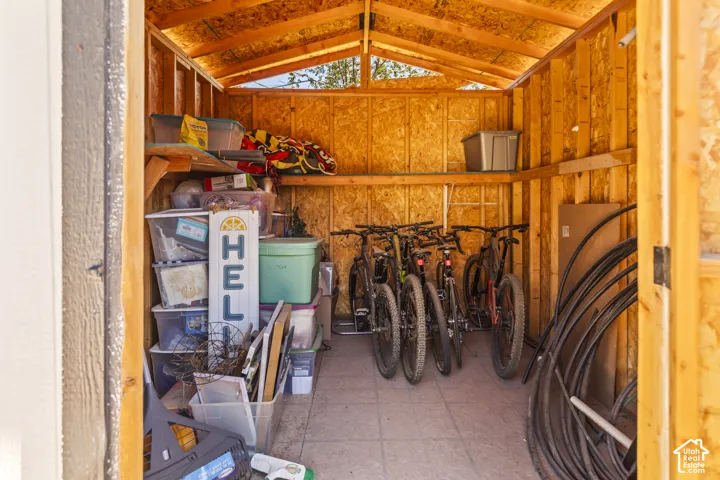 Storage structure featuring exposed wood-stud framing, integrated wall-mounted shelving, and paved flooring