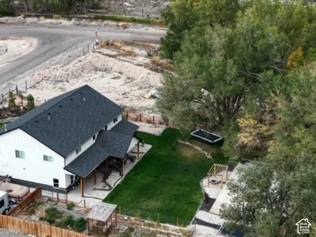 Aerial perspective of a two-story residence featuring a covered patio, a manicured lawn, a wooden pergola, and mature trees