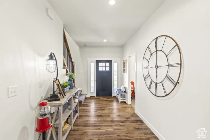 Entryway featuring wood-finish flooring, a dark-toned front door with glass panes, sidelights, and a staircase with a metal railing