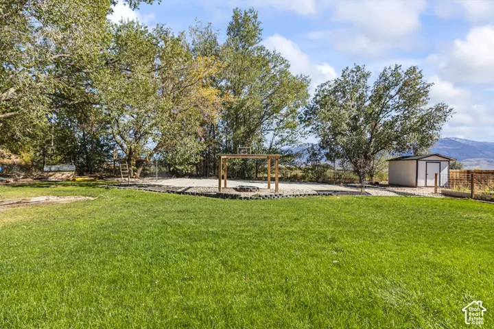 Expansive yard featuring a manicured lawn, stone-bordered gravel area, wood-frame structure, detached storage shed, and mature trees
