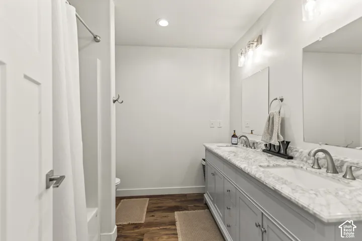Double vanity with stone-patterned countertop, dual undermount sinks, wood-finish flooring, and recessed lighting