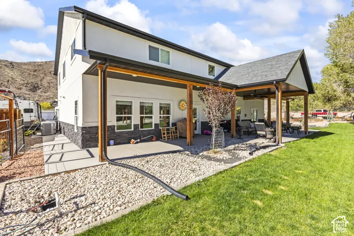 Two-story exterior featuring a light-colored stucco finish with stacked stone veneer, an expansive covered patio, wood support posts, and mountain scenery