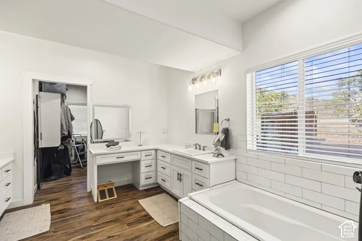 Bathroom featuring wood-finish flooring, white built-in cabinetry with integrated vanity seating, a rectangular undermount sink, and a deep soaking tub with white subway tile surround