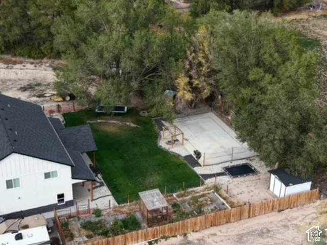 Aerial perspective of a backyard featuring a fenced-in concrete sports court, a manicured lawn, an enclosed raised-bed garden, and a detached storage structure