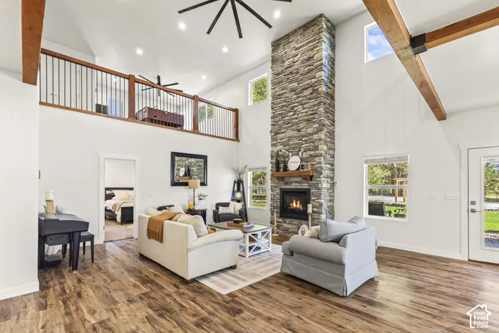 Vaulted ceilings with exposed wood beams, floor-to-ceiling stone fireplace, open-concept interior, wood-finish flooring, and a mezzanine level with metal spindle railings
