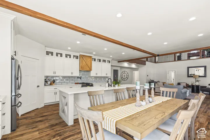Kitchen featuring white shaker-style cabinetry, a central island with quartz countertops, subway tile backsplash, and exposed natural wood ceiling beams