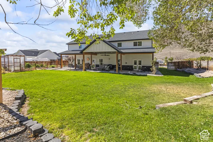 Expansive backyard featuring a manicured lawn, a covered concrete patio with wood-post support beams, mountain scenery, and a fenced perimeter