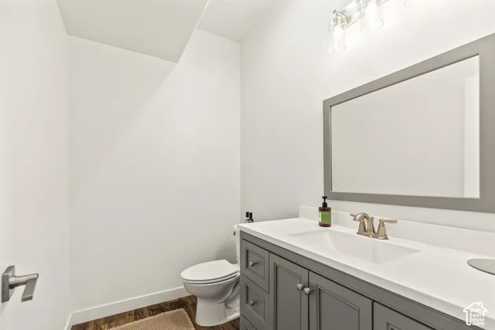 Bathroom featuring a gray vanity with a white countertop, integrated rectangular sink, brushed nickel faucet, framed wall mirror, and wood-finish flooring