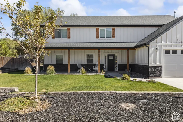 Two-story exterior featuring white board-and-batten siding, dark stone veneer accents, wood-post porch supports, and decorative wood window shutters