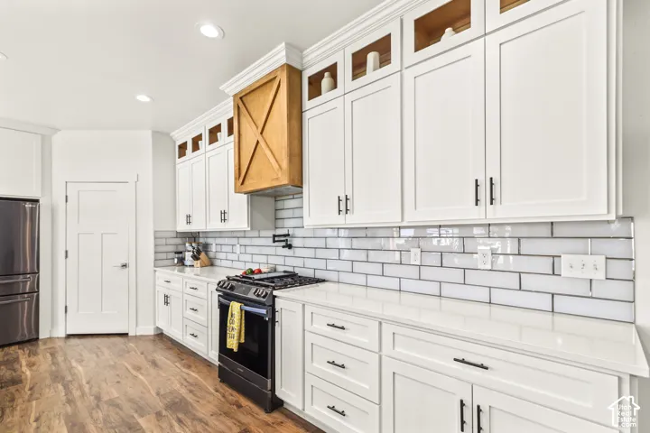 Kitchen featuring white shaker-style cabinetry with upper glass-front accents, quartz countertops, a horizontal subway tile backsplash, a custom wood range hood, and wood-finish flooring