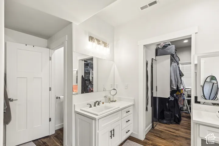 Bathroom featuring a white vanity cabinet with drawers, a rectangular undermount sink, a solid-surface countertop, and a multi-bulb light fixture above a wall-spanning mirror