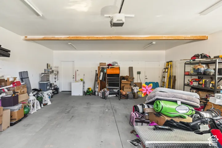Multi-car garage featuring exposed structural beam, concrete flooring, overhead automatic garage door opener, and multiple flush-mount light fixtures