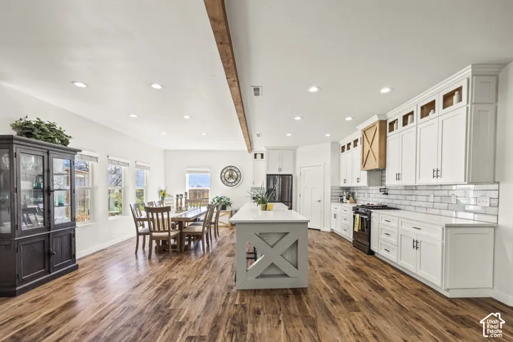 Kitchen featuring white shaker-style cabinetry, an expansive central island with X-detailing, subway tile backsplash, recessed ceiling lighting, and wood-finish flooring