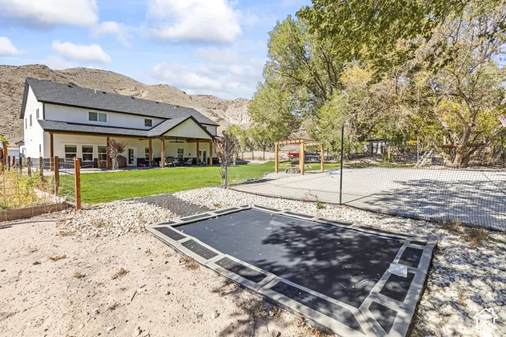 Rear exterior featuring a covered patio, an in-ground trampoline, a concrete sport court with a pergola, and mountain scenery