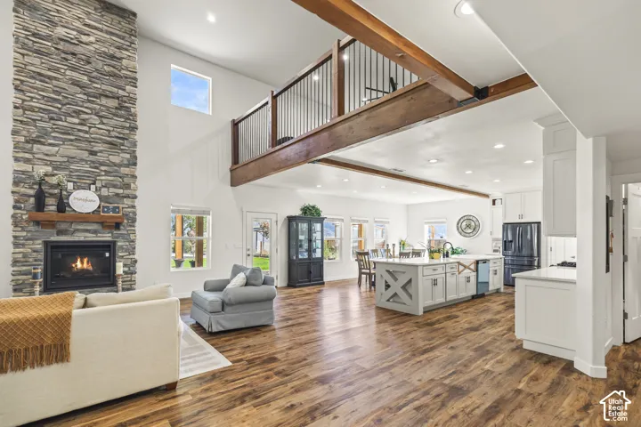 Floor-to-ceiling stone fireplace, wood-finish flooring, exposed wooden ceiling beams, center kitchen island with cabinetry, and an open mezzanine with metal balusters