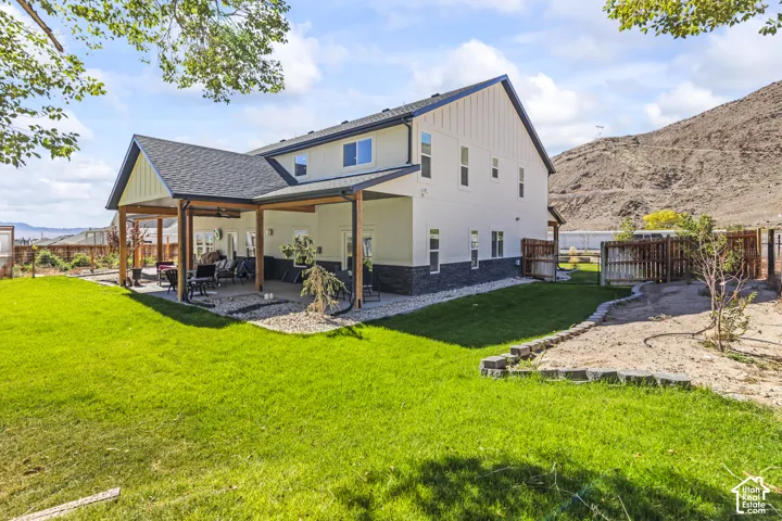 Exterior featuring a covered patio, two-tone siding with stone veneer accents, and a fenced backyard against a mountain backdrop