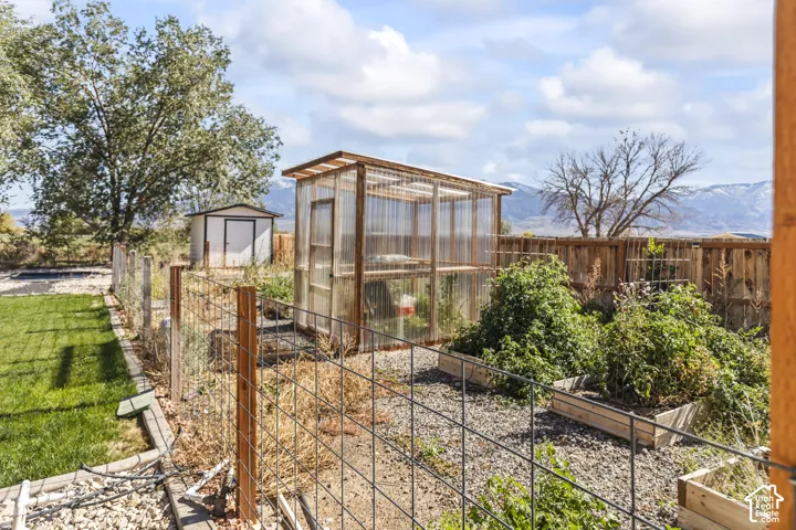 Outdoor space featuring a transparent greenhouse, raised garden beds, wood-slat fencing, a storage shed, and a gravel ground surface