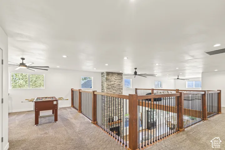 Open loft area featuring a central floor-to-ceiling stone-clad fireplace, dark wood railings with black metal balusters, recessed lighting, and ceiling fans