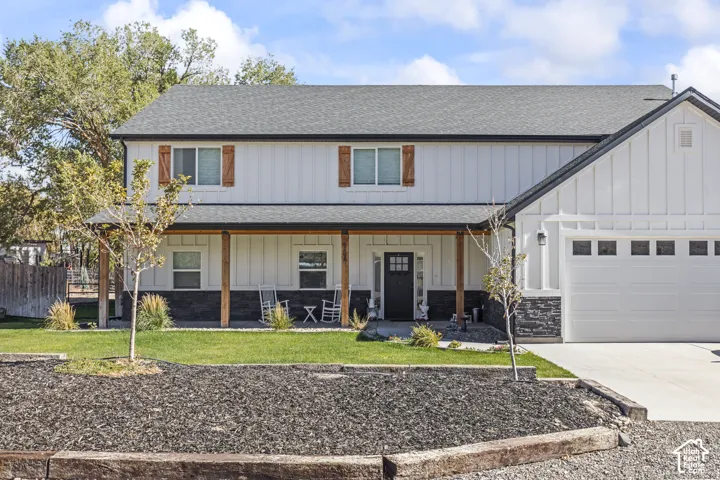 Two-story exterior featuring white board-and-batten siding, dark stone veneer accents, wood-finish window shutters, and a covered front porch with timber-frame support posts