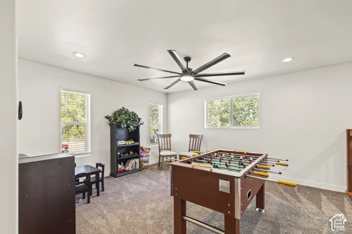 Neutral-toned interior space featuring recessed ceiling lighting, wall-to-wall carpeting, multiple windows, and a large multi-blade ceiling fan